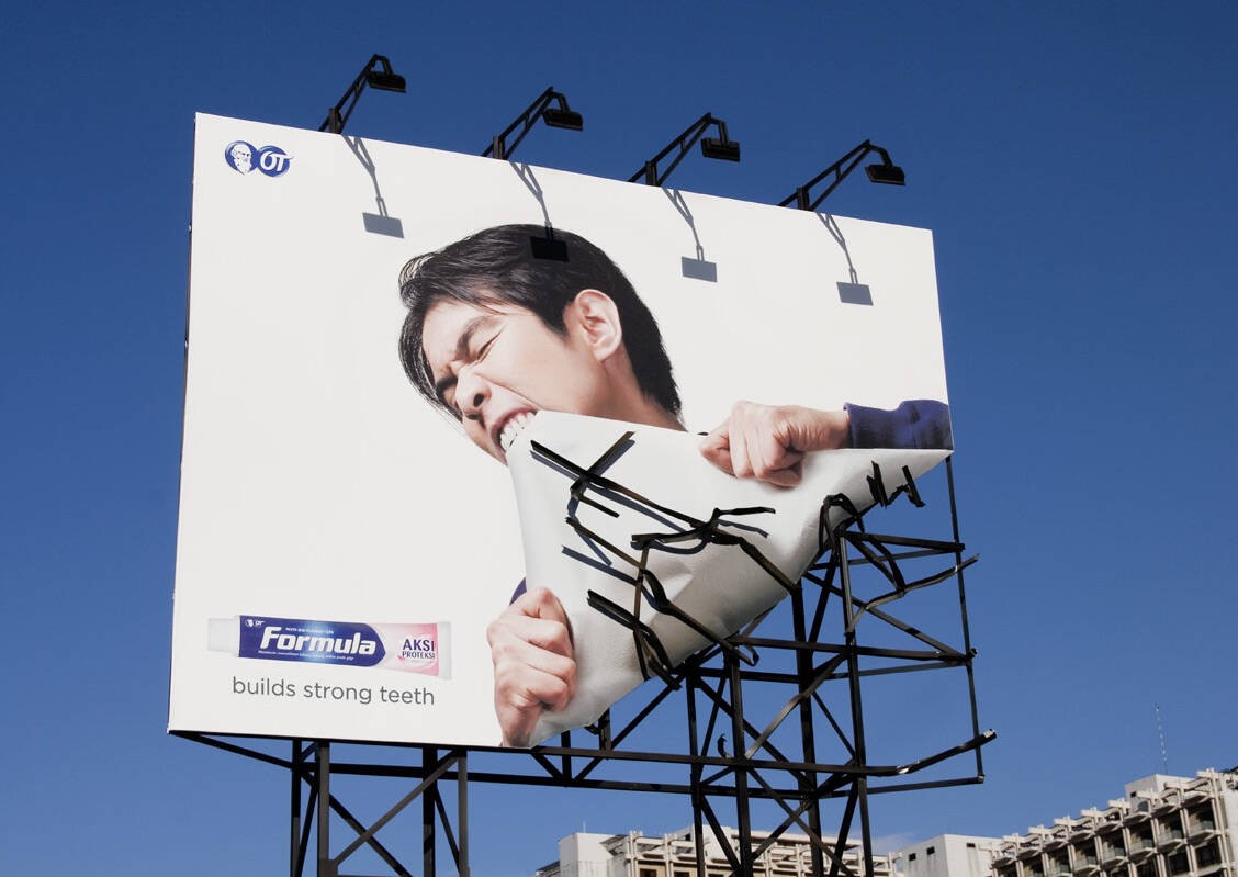A billboard for Formula toothpaste in which a man appears to be ripping off a corner of the  advertisement with his teeth.