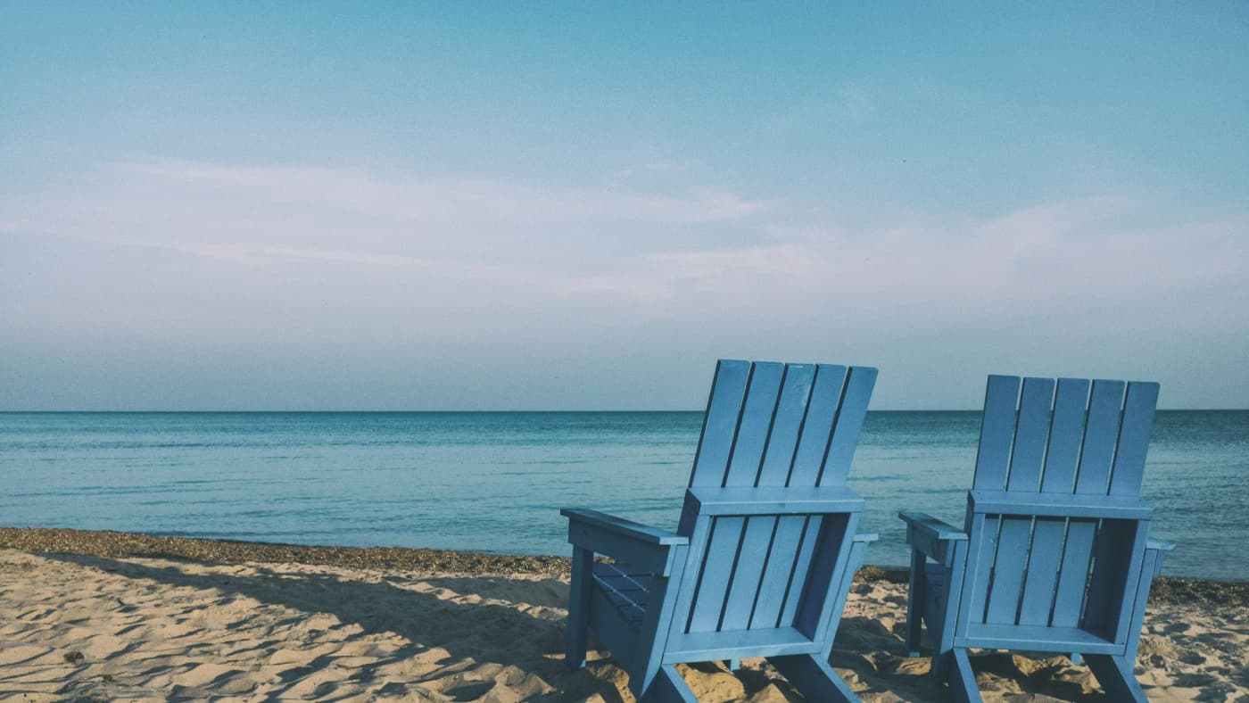 Two blue beach chairs in the sand in front of the sea